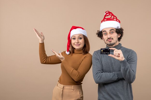 L'humeur de Noël avec excité heureux couple cool émotionnel portant des chapeaux de père Noël rouge montrant la carte bancaire