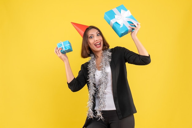 Photo gratuite l'humeur de noël avec une femme d'affaires excitée en costume avec un chapeau de noël montrant son cadeau sur jaune