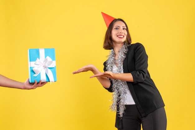 L'humeur de Noël avec une femme d'affaires souriante en costume avec un chapeau de Noël pointant la main tenant un cadeau sur le jaune