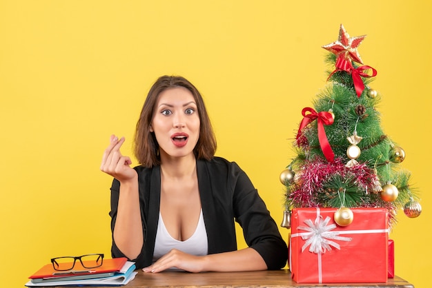 Humeur de Noël avec jeune belle femme concentrée faisant le geste de l'argent et assis au bureau