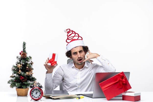 Humeur de Noël avec jeune homme d'affaires avec chapeau de père Noël et tenant son cadeau faisant appelez-moi geste sur fond blanc