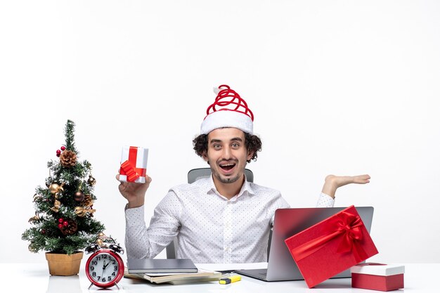 Humeur de Noël avec souriant jeune homme d'affaires avec chapeau de père Noël et tenant son cadeau joyeusement sur fond blanc