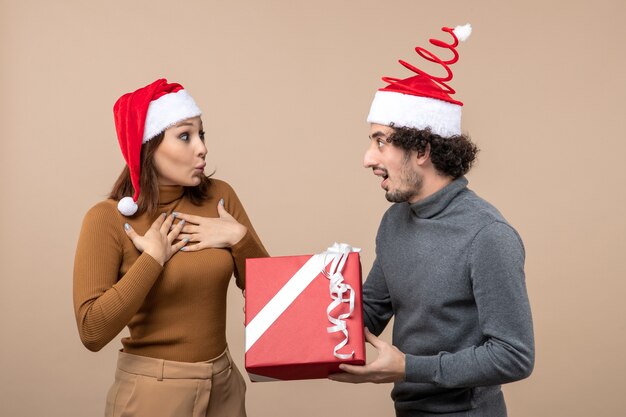 Humeur de nouvel an avec drôle excité beau couple portant des chapeaux de père Noël rouge sur fond gris