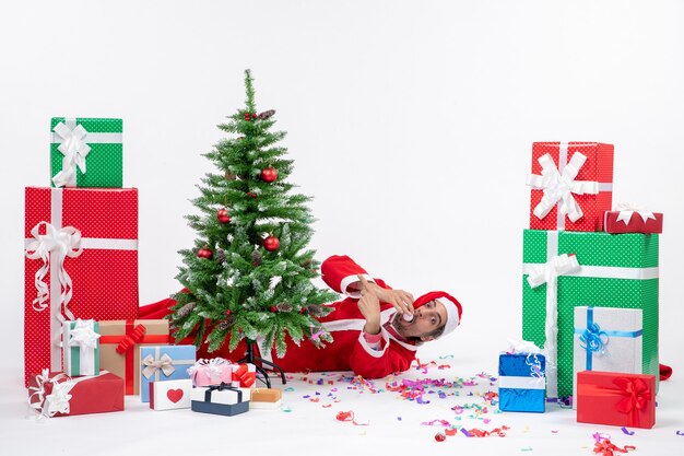 L'humeur de vacances festives avec le jeune père Noël couché derrière l'arbre de Noël près de cadeaux sur l'image de fond blanc