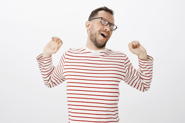 Photo gratuite il est temps de se battre après une journée de travail productive. portrait d'homme européen attrayant détendu fatigué en chemise rayée, tirant les mains en arrière tout en stratching et bâillement