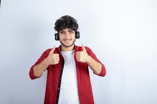 Image de beau jeune homme dans les écouteurs écoutant une chanson sur un mur blanc.