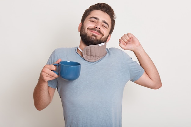 Photo gratuite image de beau mâle a le café du matin, dort encore, bâille, debout à l'intérieur isolé sur blanc