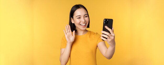 Image d'une belle fille asiatique heureuse en train de discuter en vidéo sur une application pour smartphone debout contre