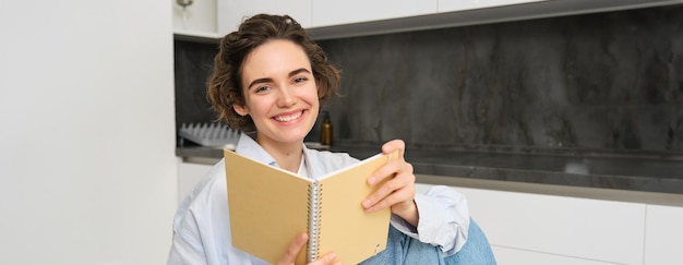Photo gratuite image d'une belle fille à la maison tenant un carnet en train de faire ses devoirs pour l'examen dans sa cuisine