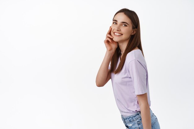 Image de belle fille toucher son visage naturel sans maquillage, sourire heureux, peau lisse et propre après avoir nettoyé les produits de beauté, concept de publicité, fond blanc