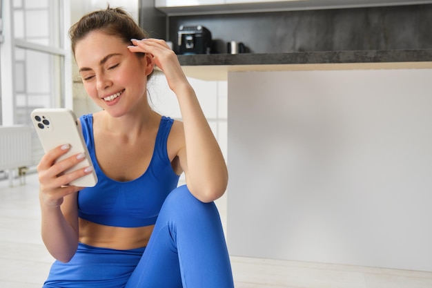 Photo gratuite image d'une belle jeune femme en forme avec un soutien-gorge bleu et des leggings regarde son entraînement sur smartphone