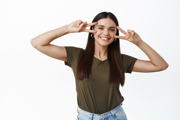 Image de la belle jeune femme avec un maquillage naturel souriant heureux montrant des signes de disco sur le visage debout sur fond blanc