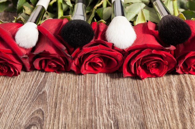 Image conceptuelle de pinceaux de maquillage à côté de roses sur fond de bois