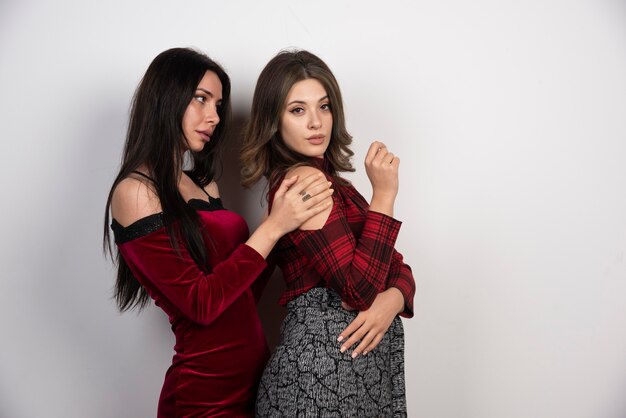 Image de deux belles jeunes filles debout et posant sur un mur blanc.