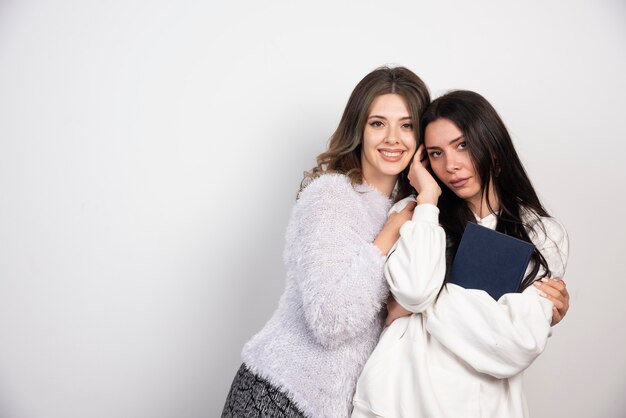 Image de deux meilleurs amis debout ensemble et posant sur un mur blanc.