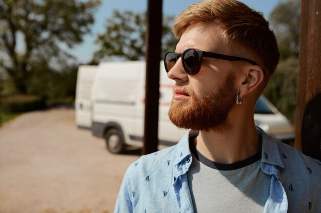 Image extérieure de beau jeune homme barbu de race blanche portant des nuances