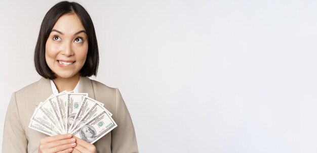 Image d'une femme d'affaires asiatique heureuse femme d'affaires montrant de l'argent en dollars et pensant debout