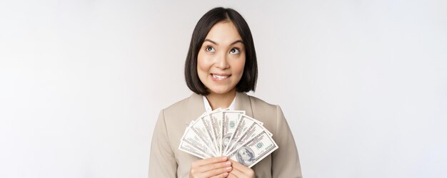 Image d'une femme d'affaires asiatique heureuse femme d'affaires montrant de l'argent en dollars et pensant debout