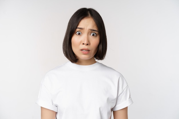 Image d'une femme asiatique choquée et frustrée qui a l'air alarmée par la caméra ne peut pas comprendre perplexe debout sur fond blanc