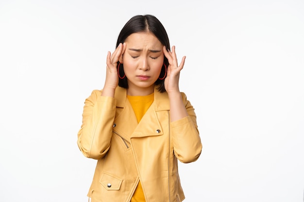 Image d'une femme asiatique massant les tempes de la tête avec un visage inquiet souffrant de migraine debout sur fond blanc