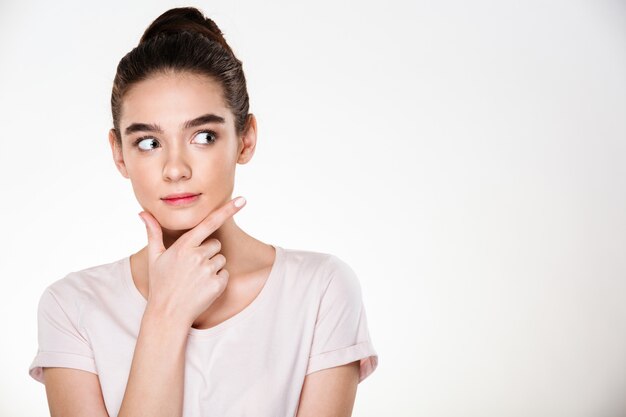 Image de femme sérieuse aux cheveux bruns en chignon touchant son menton en pensant ou en pesant le pour et le contre posant