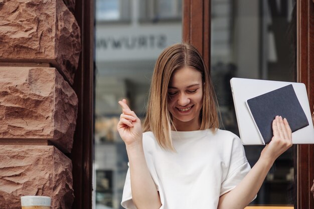 Image d'une femme souriante avec des cahiers dans la rue croisant les doigts