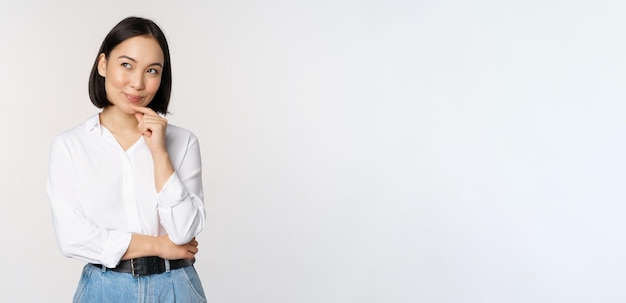 Photo gratuite image d'une femme souriante réfléchie a une idée de planification intrigante regardant de côté et pensant debout dans un chemisier blanc de bureau sur fond de studio