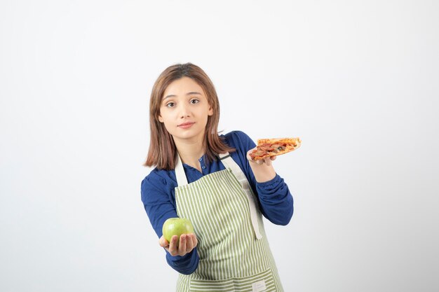 Image d'une femme en tablier essayant de choisir quoi manger pomme ou pizza