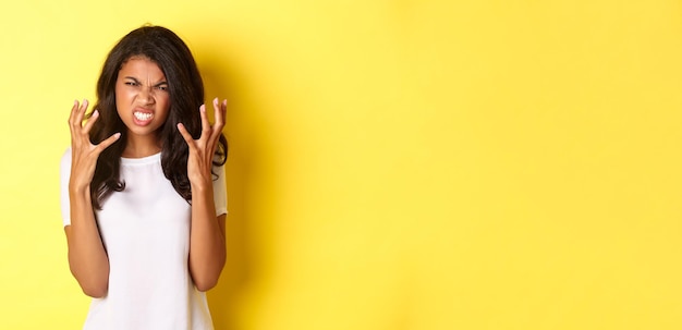 Photo gratuite image d'une fille afro-américaine frustrée et en colère grimaçant et se serrant la main folle debout sur yel