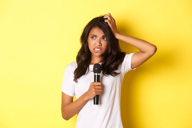 Image d'une fille afro-américaine indécise tenant un microphone et semblant hésitante debout