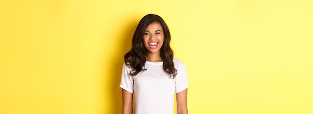 Image d'une fille afro-américaine insouciante en t-shirt blanc montrant la langue souriante et clignant de l'œil heureux stan