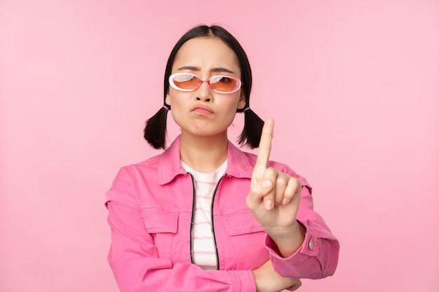 Photo gratuite image d'une fille asiatique élégante et sérieuse dans des lunettes de soleil montrant un signe d'arrêt interdisant le geste tabou disant non debout sur fond rose