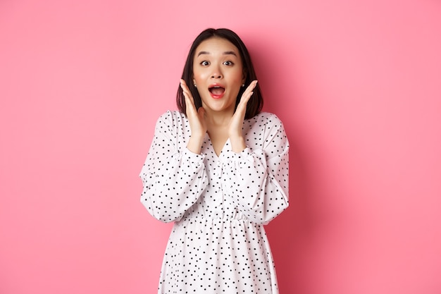 Image d'une fille coréenne surprise en robe modèle féminin regardant la caméra et haletant amazd debout devant ...