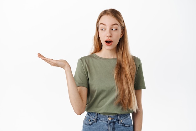 Image d'une fille excitée regarde sa main tenant un fond avec un élément d'affichage d'intérêt sur la paume ouverte debout sur fond blanc Concept de publicité