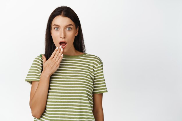 Image d'une fille qui a l'air excitée et surprise de couvrir la bouche en entendant une rumeur intéressante debout en t-shirt sur fond blanc