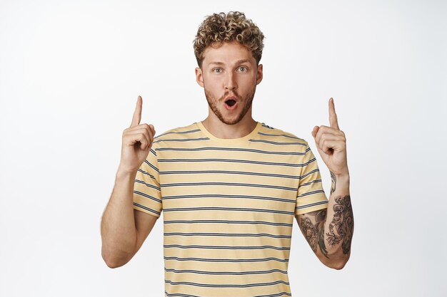 Image d'un gars heureux surpris pointant les doigts vers le texte promotionnel montrant votre logo ou signe vers le haut debout en t-shirt sur fond blanc faisant l'annonce