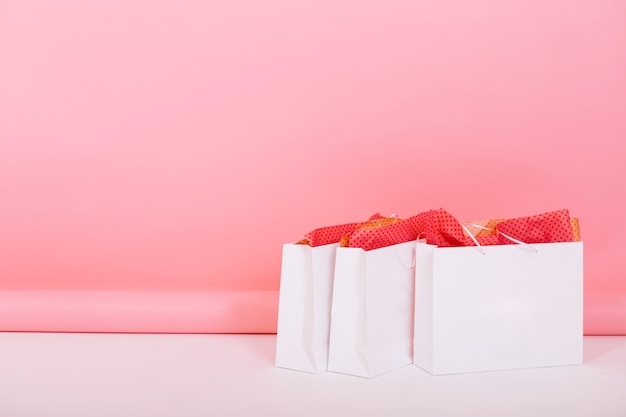 Image de grands sacs en papier du magasin avec des emballages-cadeaux d'ornement à l'intérieur debout sur le sol sur fond rose. Quelqu'un a préparé des cadeaux romantiques pour l'anniversaire du mariage en les laissant dans la chambre