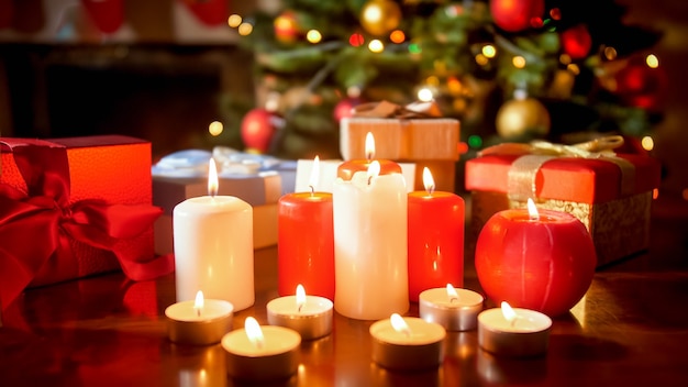 Image en gros plan de beaucoup de bougies allumées et de cadeaux contre un sapin de noël rougeoyant dans le salon