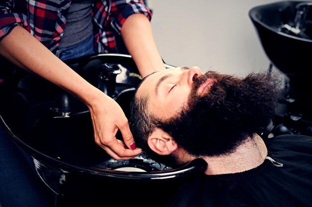 Image en gros plan d'une coiffeuse lavant les cheveux d'hommes barbus avant la coupe de cheveux dans un salon.