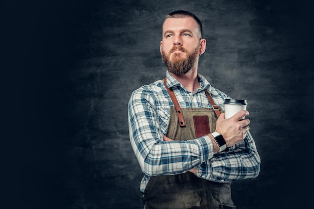 Image en gros plan d'un homme barbu roux tenant une tasse de café sur fond gris.