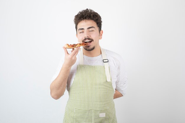 Image d'un homme cuisinier mangeant une tranche de pizza sur blanc