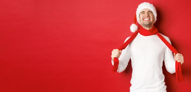 Image d'un homme en détresse et frustré en bonnet de noel, se calant avec un foulard de tristesse, debout sur fond rouge.