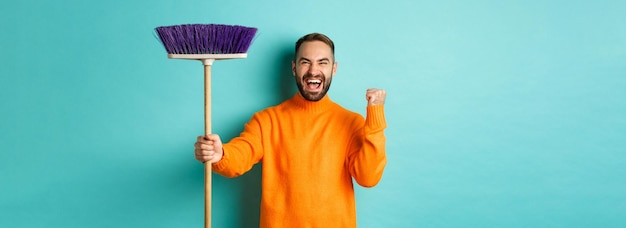 Photo gratuite image d'un homme encouragé et motivé se préparant pour le nettoyage en tenant un balai et en faisant une pompe à poing