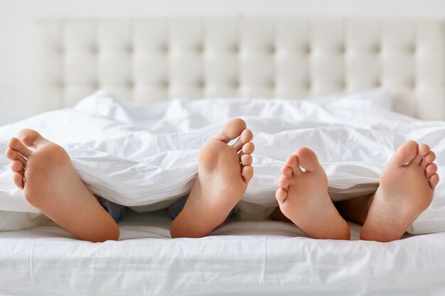 Image d'homme et femme pieds nus sous une couverture dans la chambre.