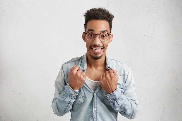 Photo gratuite image d'homme gai avec visage ovale, porte des lunettes rondes, déchire la chemise,