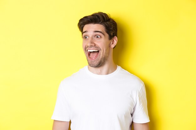 Image d'un homme heureux vérifiant la promo, regardant à gauche avec étonnement, debout en t-shirt blanc sur fond jaune.