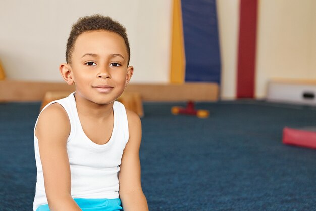 Photo gratuite image intérieure d'adorable écolier afro-américain positif en sportswear smiling at camera