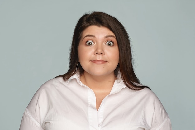 Image isolée d'une femme gérante de taille plus aux yeux d'achat drôle en chemise formelle blanche exprimant son étonnement, regardant en pleine incrédulité, choquée par des nouvelles ou des potins inattendus. Surprise et choc