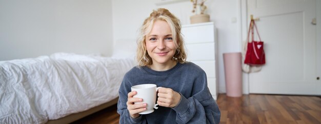 Photo gratuite image d'une jeune adolescente assise dans sa chambre au sol en train de boire une tasse de thé et de profiter de la journée à