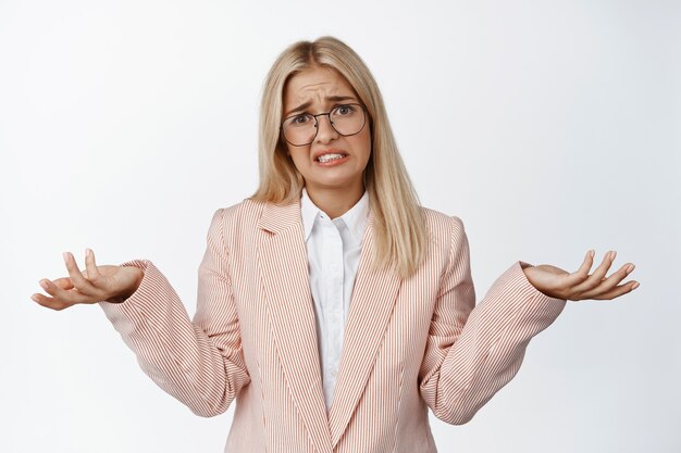 Image d'une jeune femme d'affaires s'excusant, haussant les épaules et ayant l'air confus, je ne sais pas, debout sur blanc.